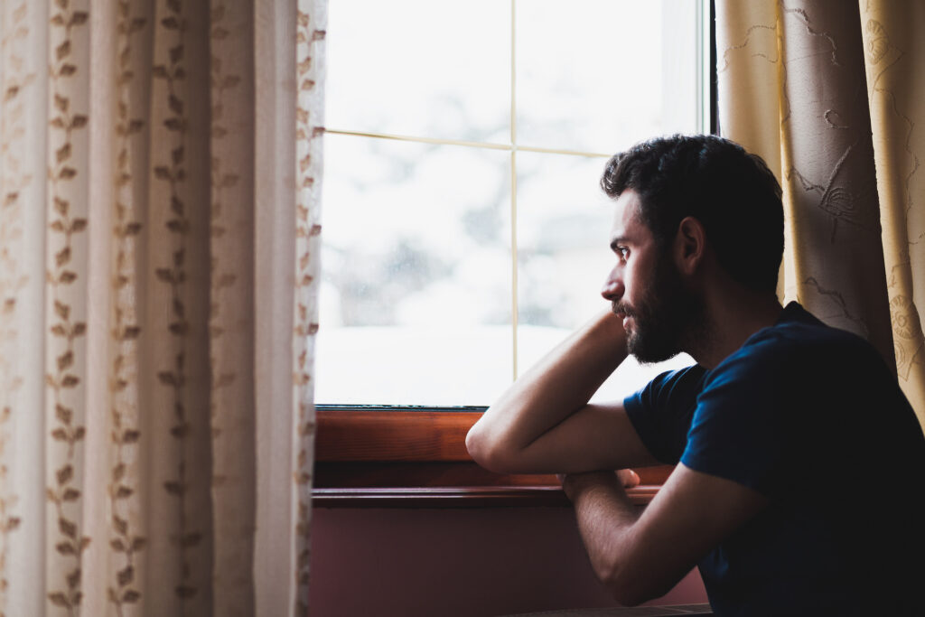 man staring out window alone and isolated.