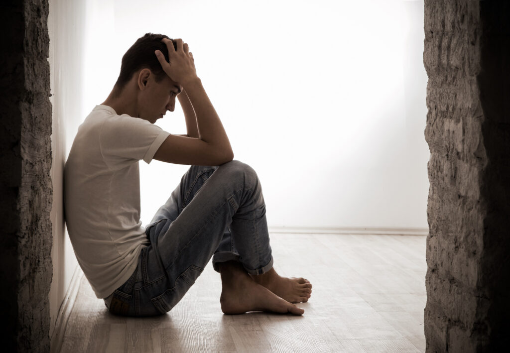 young man sitting on floor holding head in his hands looking sad