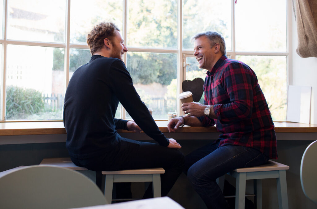 two men sitting and laughing in coffee shop on an addiction recovery journey