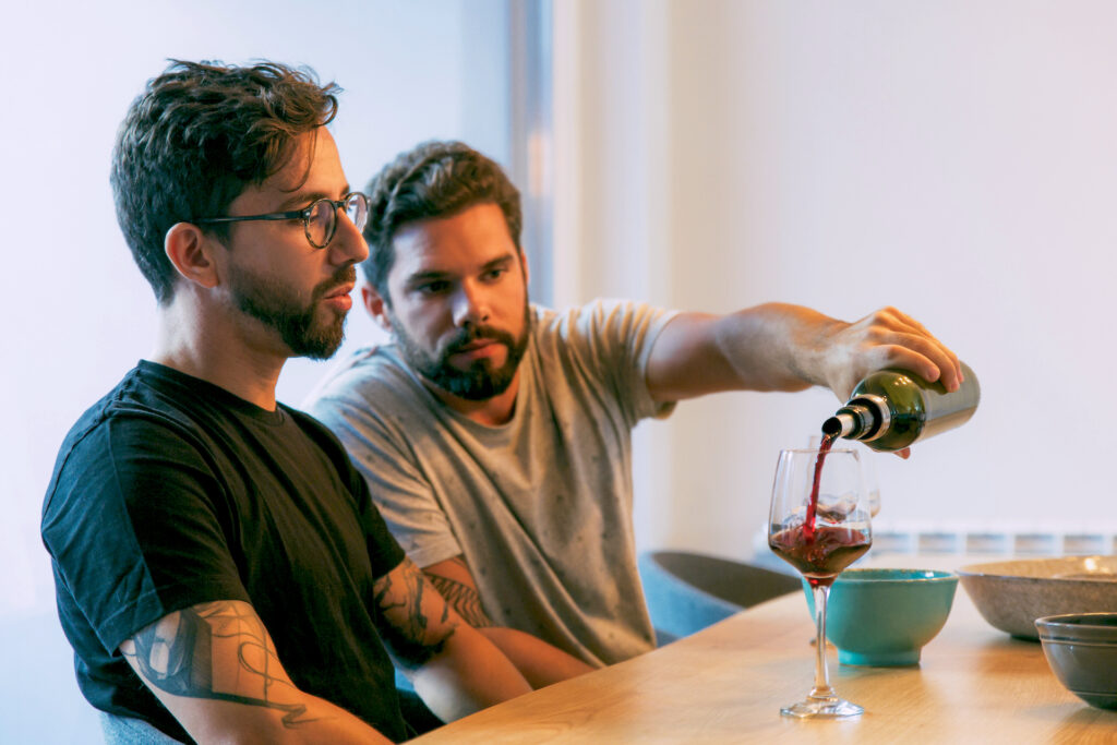 one man pouring wine into another's glass making his addiction recovery difficult