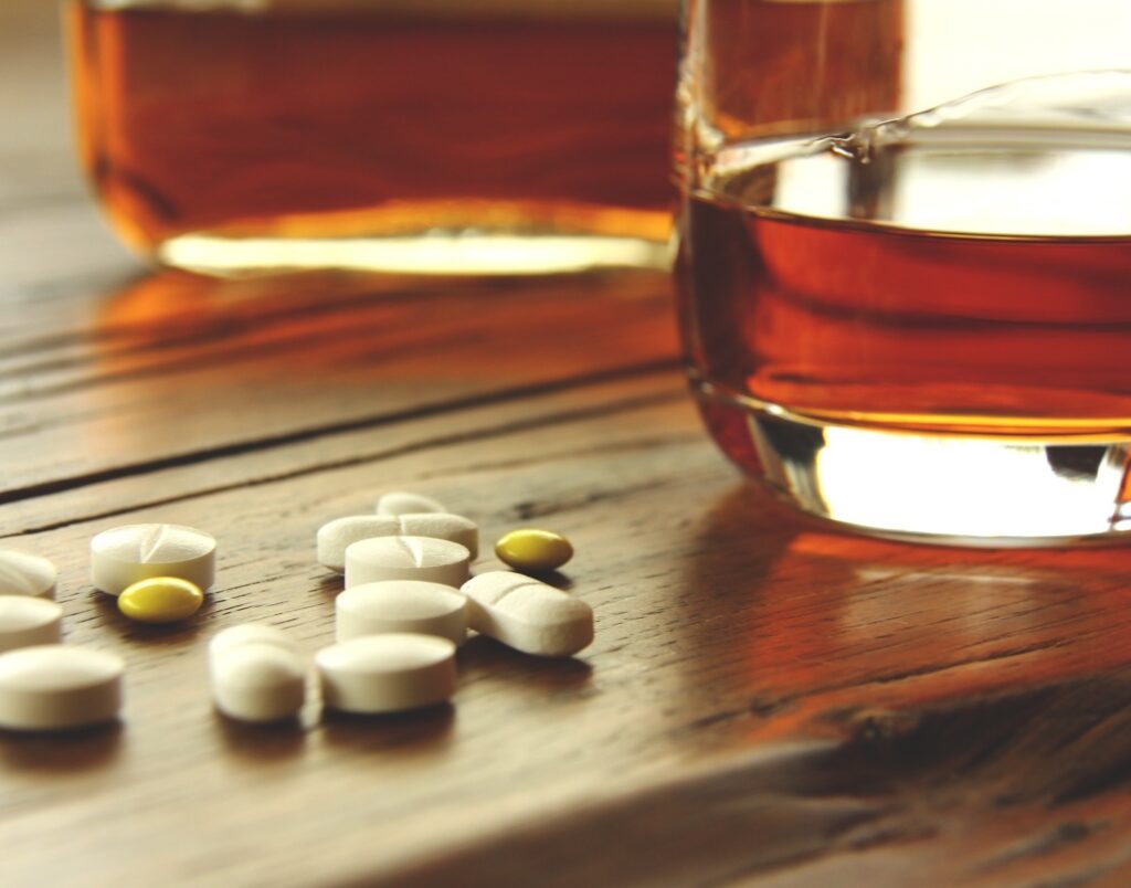 glass of alcohol next to prescription pills symbolising polysubstance use