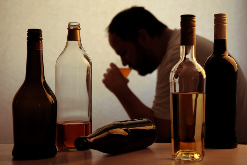 man drinking with bottles of alcohol in foreground symbolising alcohol awareness